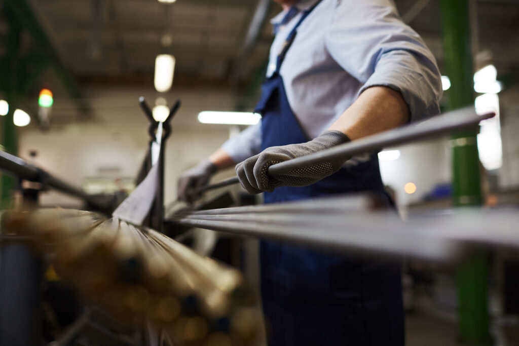 Close-up of manual worker in overalls holding metal pipe while working in the plant